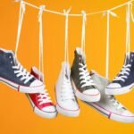 Stylish sneakers in various colors hanging with laces on a vivid orange backdrop. Ideal for fashion themes.