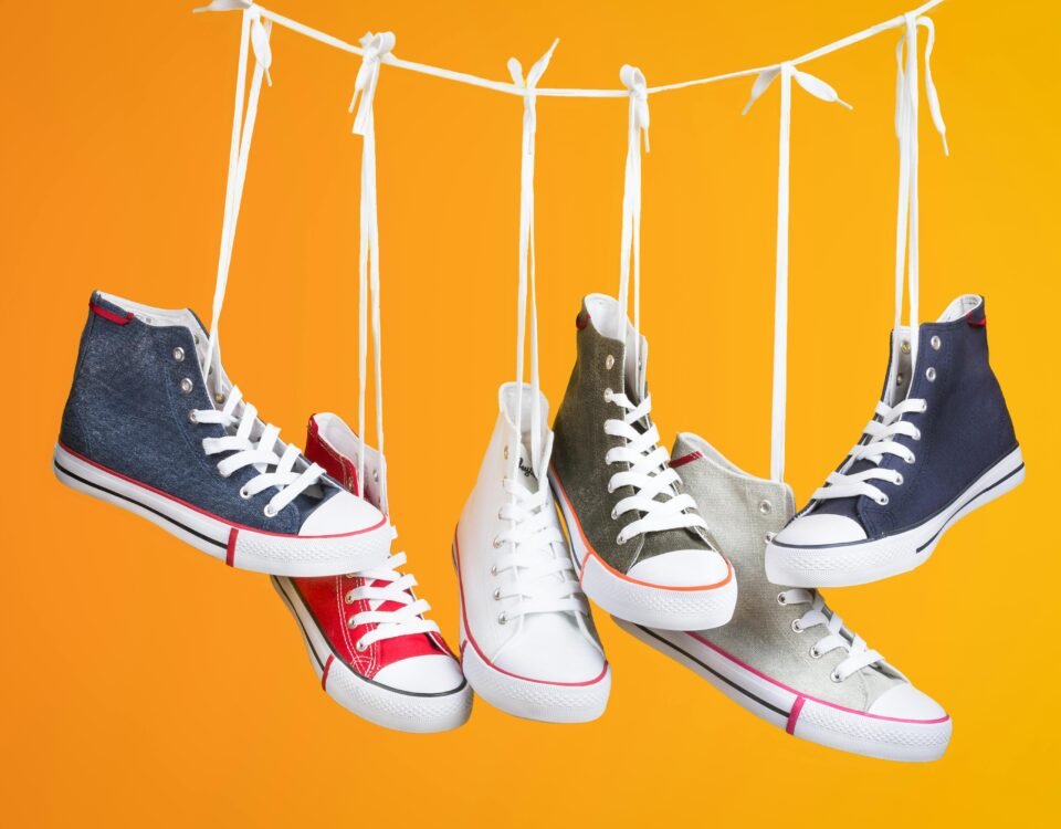 Stylish sneakers in various colors hanging with laces on a vivid orange backdrop. Ideal for fashion themes.